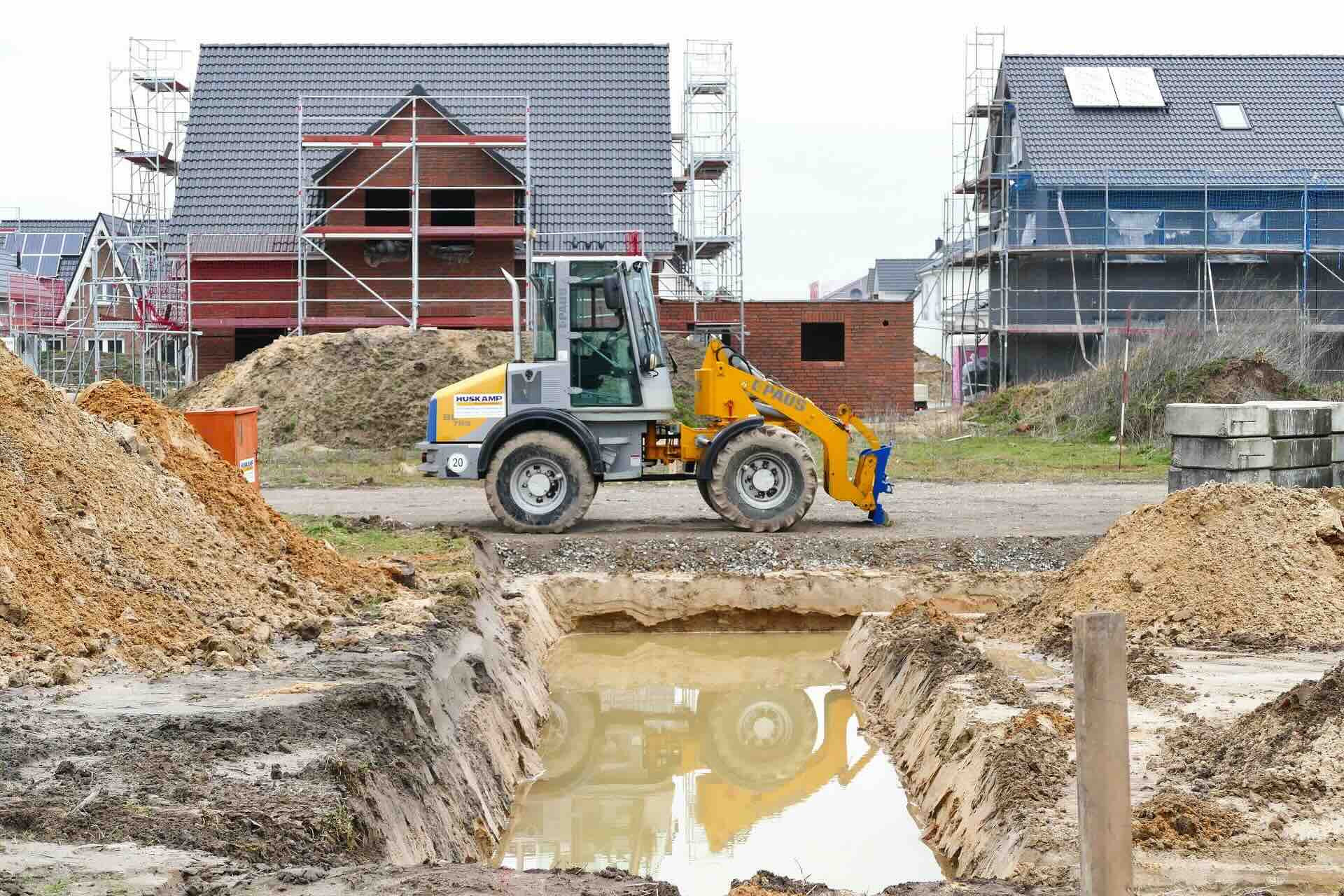 Shovel rijdt tussen woningen in aanbouw op een bouwplaats.
