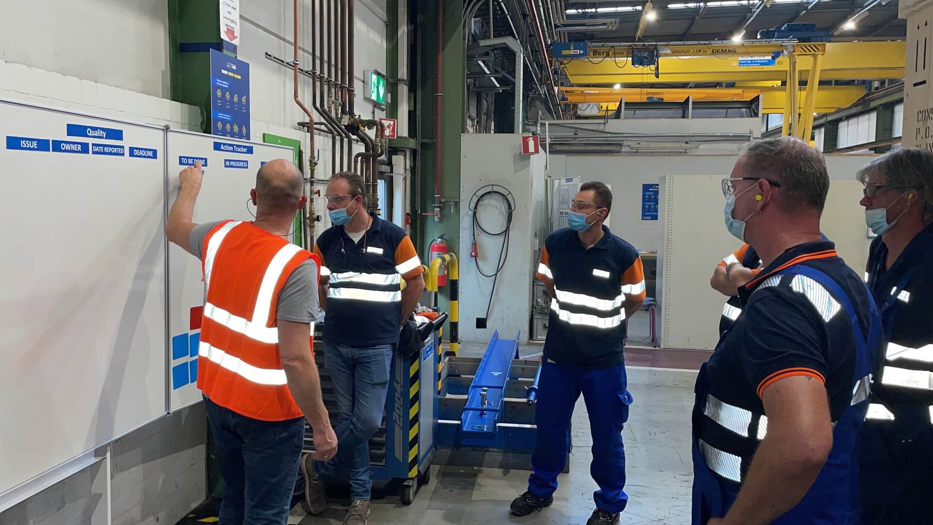 Medewerkers bespreken actiepunten bij het verbeterbord in de werkplaats.