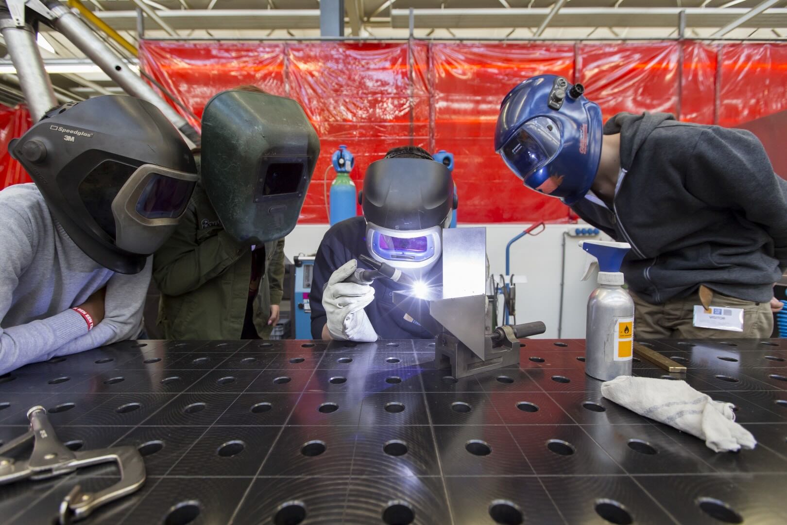 Medewerkers oefenen laswerk aan een metalen onderdeel in een werkplaats.