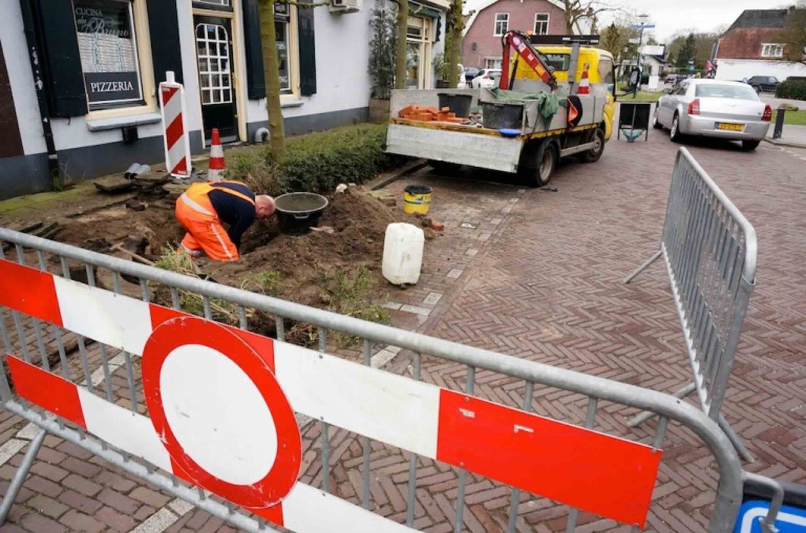 Monteur voert rioolwerkzaamheden uit in een straat die is afgezet voor verkeer.