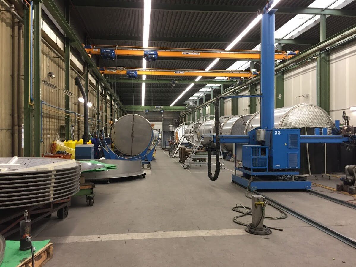 Productiehal met grote metalen tanks en apparatuur voor tankbouw.