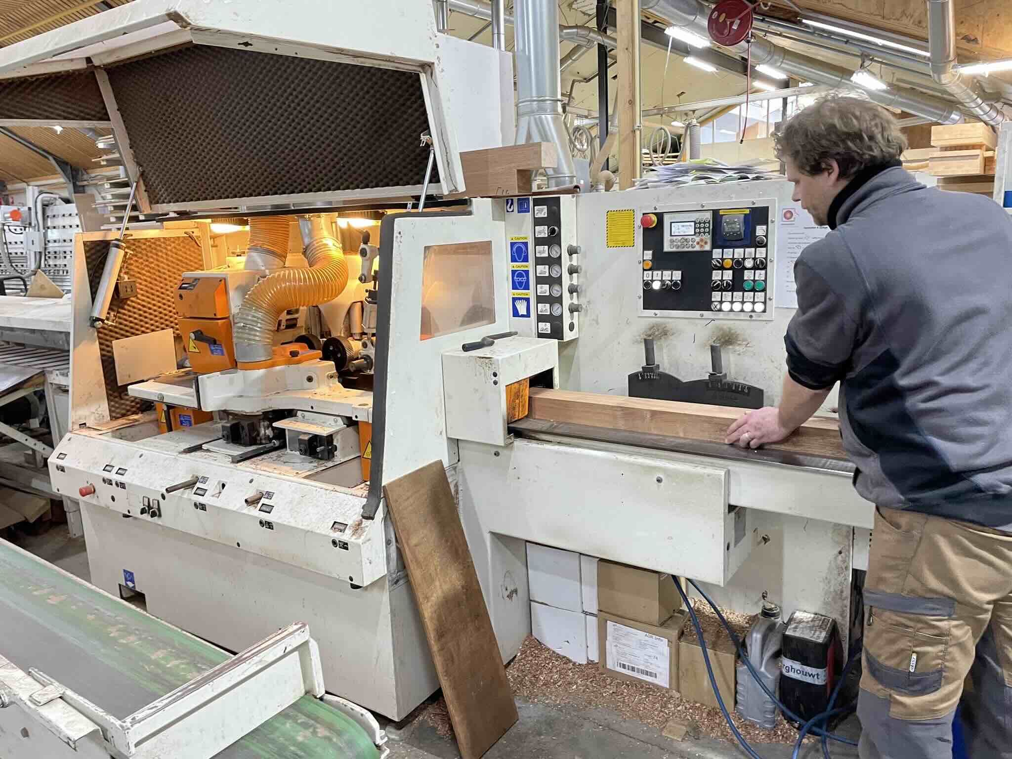 Medewerker voert een houten balk in een houtbewerkingsmachine.