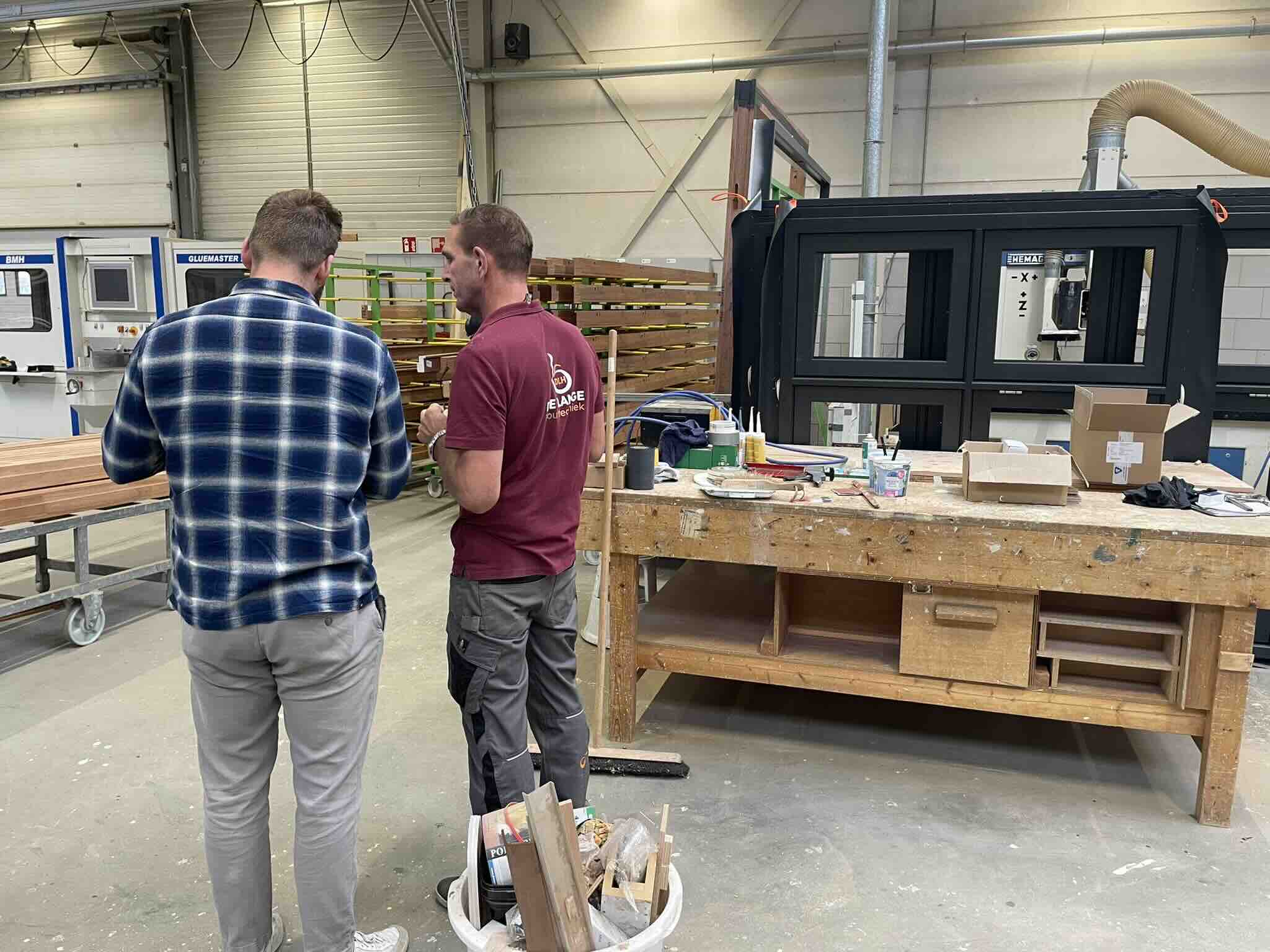 Twee medewerkers bespreken het werk naast een machine in een timmerwerkplaats.