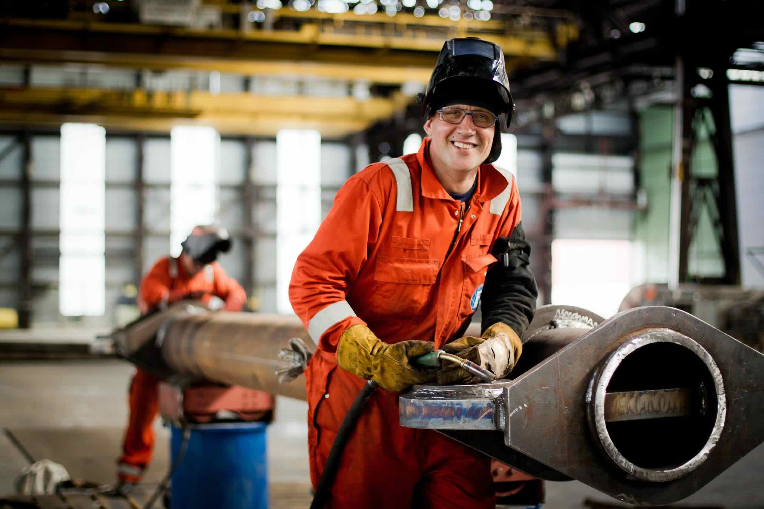 Medewerker in oranje werkkleding werkt met gereedschap aan een metalen constructie.