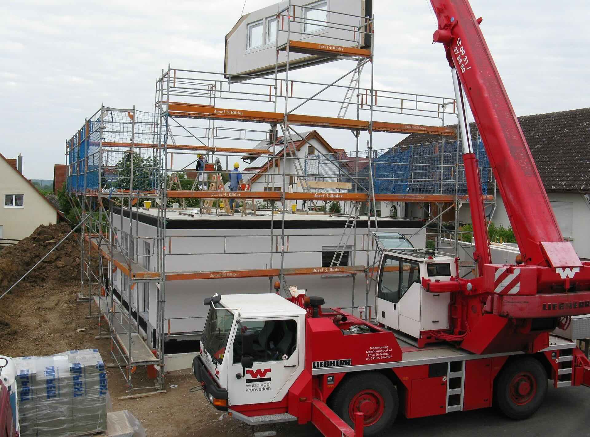 Bouwvakkers werken aan een woning in aanbouw naast een bouwkraan.