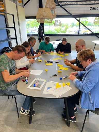 Deelnemers maken aantekeningen en werken samen aan trainingsopdrachten aan een tafel.