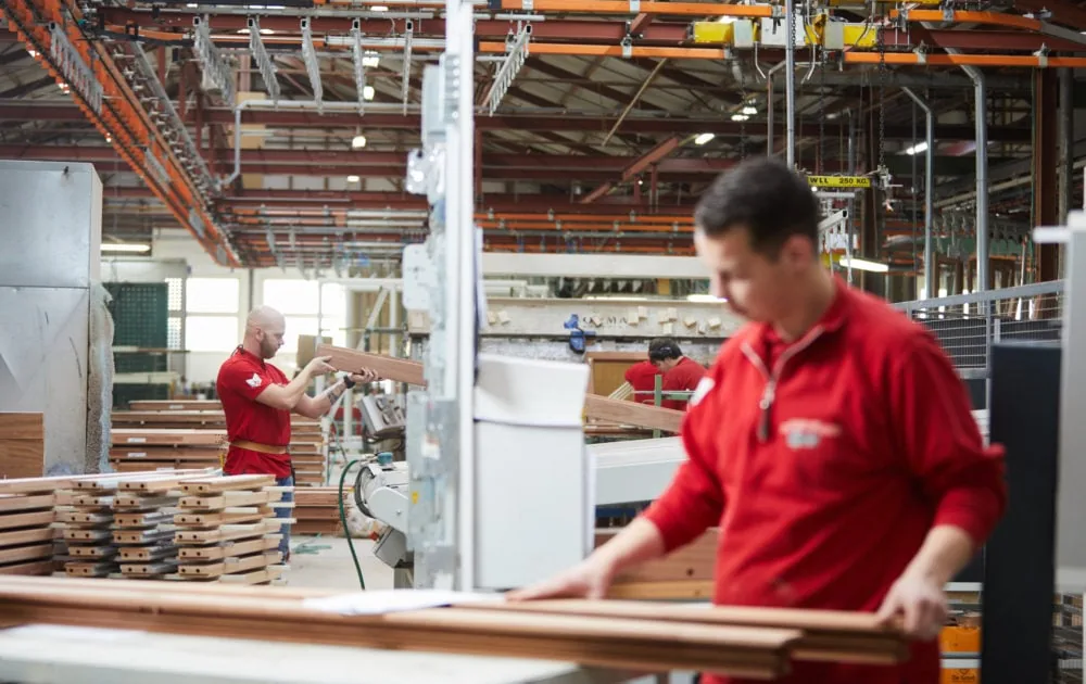 Medewerkers verwerken houten onderdelen aan een werktafel in een timmerwerkplaats.