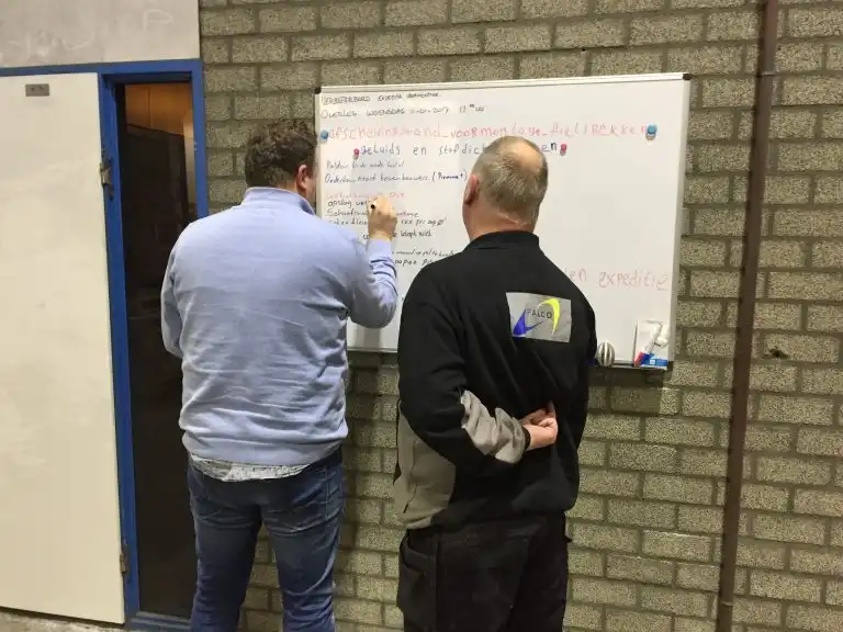 Twee medewerkers bespreken verbeterpunten bij een whiteboard in de werkplaats