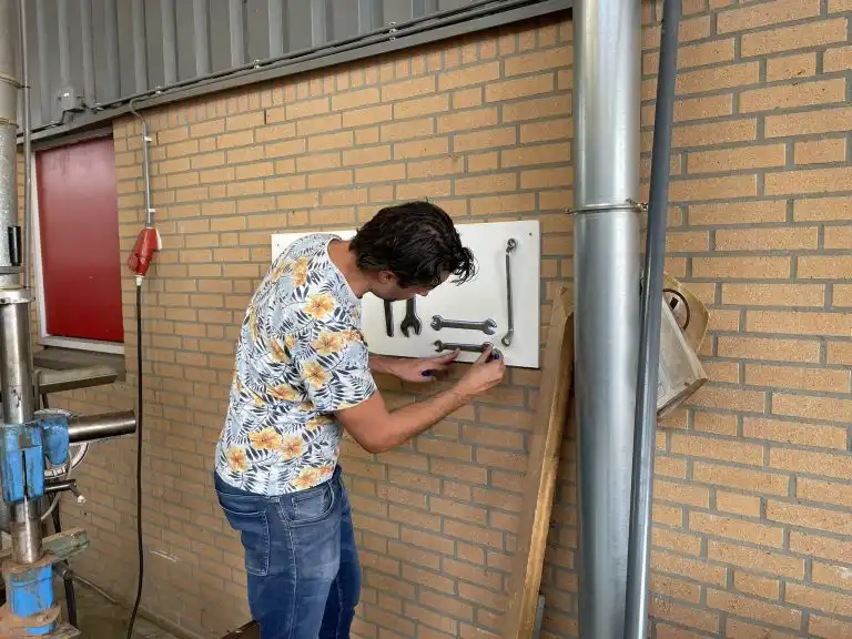 Deelnemer tekent de omtrek van gereedschap op een schaduwbord in de werkplaats.